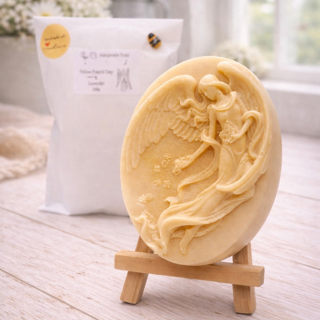 An oval-shaped handmade vegan soap, featuring an intricate relief carving of a guardian angel with large wings holding flowers, displayed on a small wooden easel.