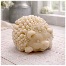 Load image into Gallery viewer, A detailed handmade vegan soap sculpted in the shape of a round, sitting hedgehog with intricate quill textures and a cute face, in a natural honey-brown tone, displayed on a light wooden surface.
