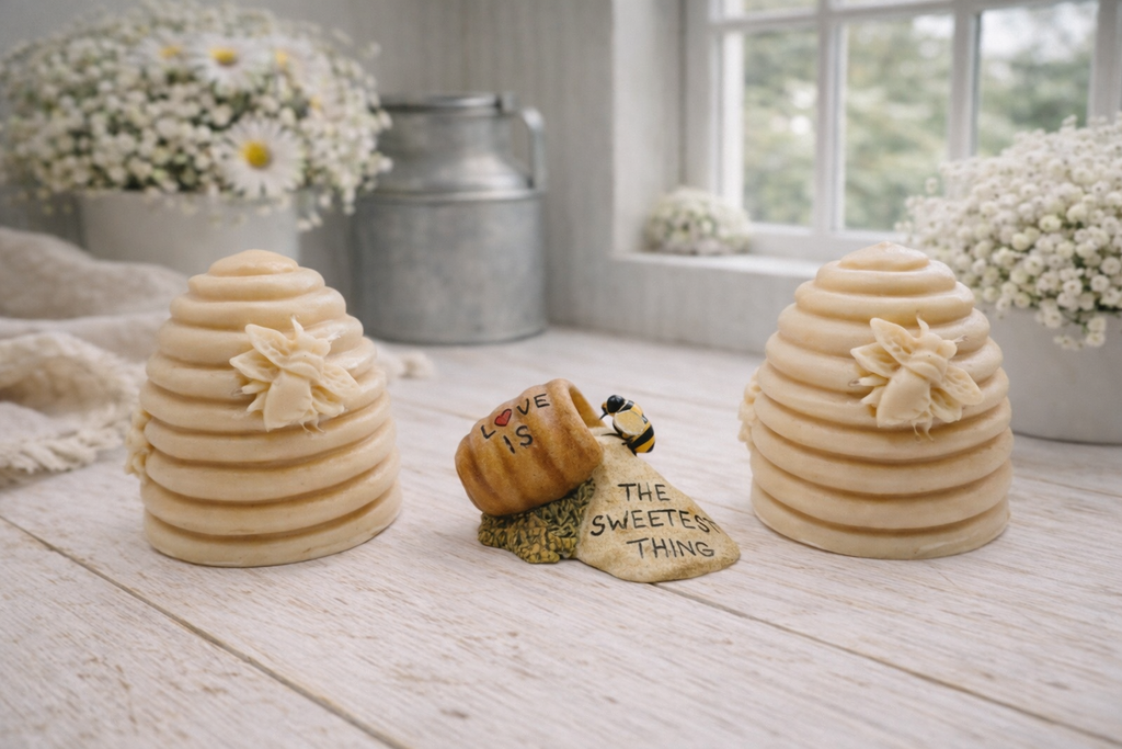 Two handmade vegan soaps sculpted into traditional dome-shaped beehives (skeps) with small bees resting on the sides, flanking a decorative centrepiece featuring a honey pot and the words "The Sweetest Thing," all displayed on a rustic wooden surface.