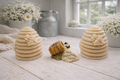 Two handmade vegan soaps sculpted into traditional dome-shaped beehives (skeps) with small bees resting on the sides, flanking a decorative centrepiece featuring a honey pot and the words "The Sweetest Thing," all displayed on a rustic wooden surface.