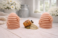 Load image into Gallery viewer, Two handmade vegan soaps sculpted into traditional dome-shaped beehives (skeps) with small bees resting on the sides, flanking a decorative centrepiece featuring a honey pot and the words "The Sweetest Thing," all displayed on a rustic wooden surface.
