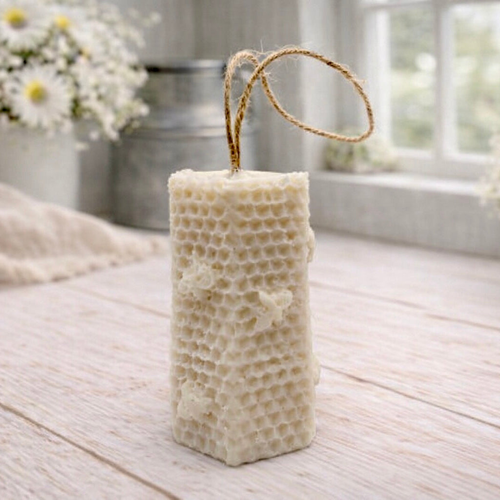 A tall, rectangular handmade vegan soap with a detailed honeycomb texture on all sides and small embossed bees, featuring a natural twine hanging rope, displayed upright on a light wooden surface.