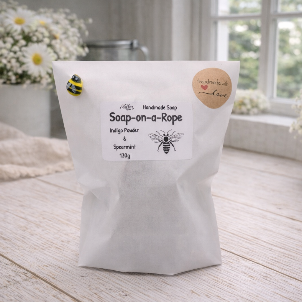 Bag of soap-on-a-rope with bee illustrations on a wooden surface with flowers in the background