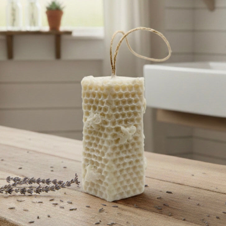 A tall, rectangular handmade vegan soap with a detailed honeycomb texture on all sides and small embossed bees, featuring a natural twine hanging rope, displayed upright on a light wooden surface.