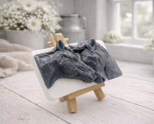 Load image into Gallery viewer, A rectangular handmade vegan soap featuring a detailed 3D relief of two horse heads leaning affectionately towards each other, finished in a slate-grey tone against a white soap base and displayed on a miniature wooden easel.
