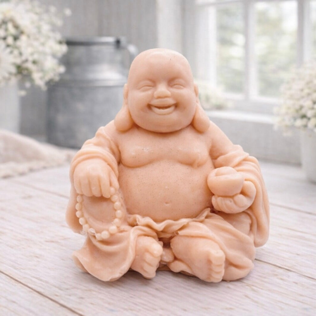 A 3D handmade vegan soap sculpted into a joyful Laughing Buddha sitting in a meditative pose, holding prayer beads and a small bowl, displayed in a bright farmhouse setting