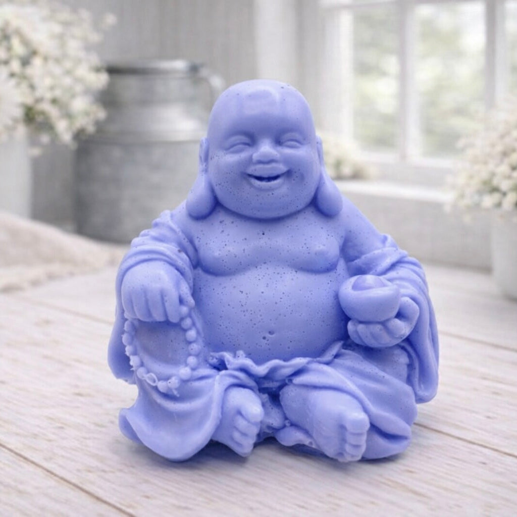 A 3D handmade vegan soap sculpted into a joyful Laughing Buddha sitting in a meditative pose, holding prayer beads and a small bowl, displayed in a bright farmhouse setting