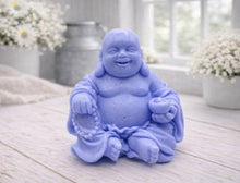 Load image into Gallery viewer, A 3D handmade vegan soap sculpted into a joyful Laughing Buddha sitting in a meditative pose, holding prayer beads and a small bowl, displayed in a bright farmhouse setting
