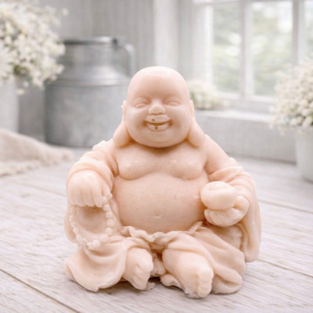 A 3D handmade vegan soap sculpted into a joyful Laughing Buddha sitting in a meditative pose, holding prayer beads and a small bowl, displayed in a bright farmhouse setting