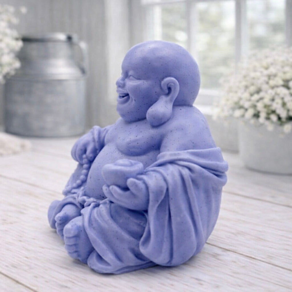 A 3D handmade vegan soap sculpted into a joyful Laughing Buddha sitting in a meditative pose, holding prayer beads and a small bowl, displayed in a bright farmhouse setting