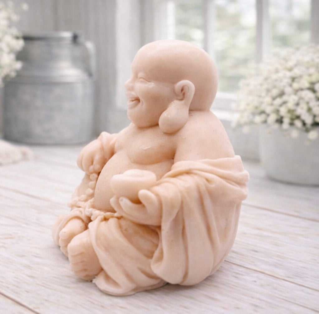 A 3D handmade vegan soap sculpted into a joyful Laughing Buddha sitting in a meditative pose, holding prayer beads and a small bowl, displayed in a bright farmhouse setting