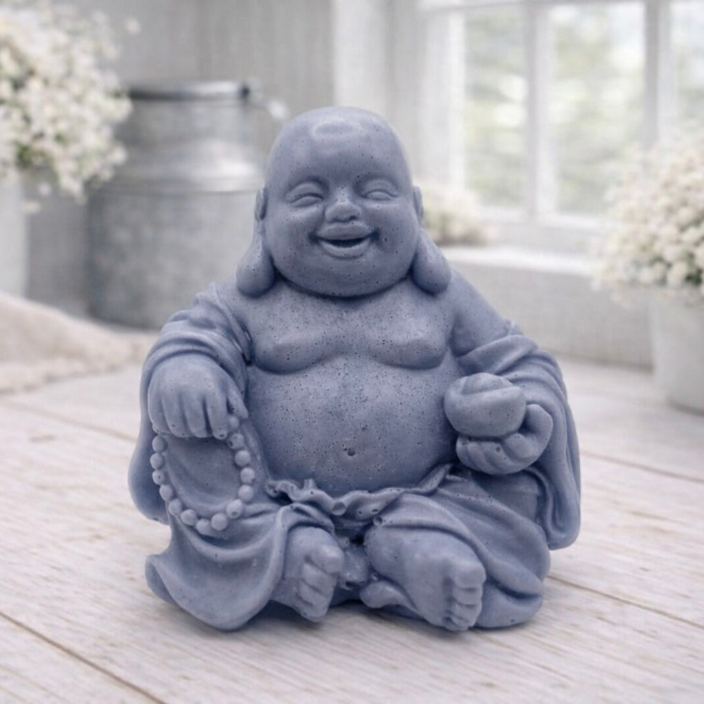A 3D handmade vegan soap sculpted into a joyful Laughing Buddha sitting in a meditative pose, holding prayer beads and a small bowl, displayed in a bright farmhouse setting