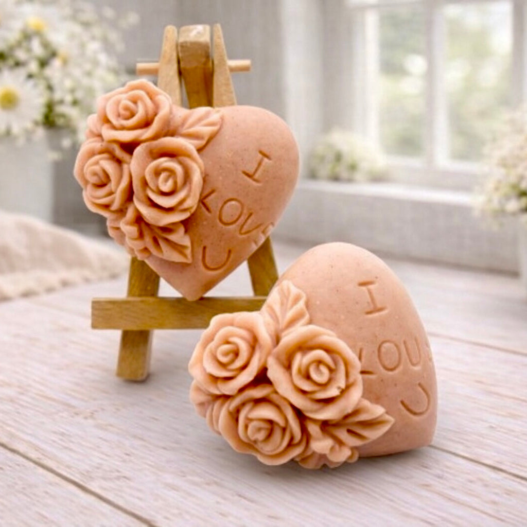 A handmade vegan soap gift set, featuring a central heart-shaped relief surrounded by a border of intricate rose flowers and delicate foliage, displayed on a small wooden easel.