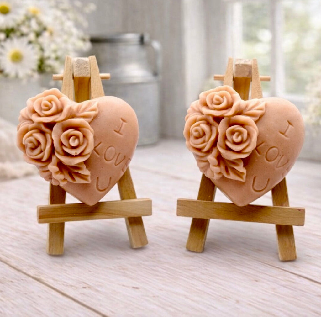 A handmade vegan soap gift set, featuring a central heart-shaped relief surrounded by a border of intricate rose flowers and delicate foliage, displayed on a small wooden easel.