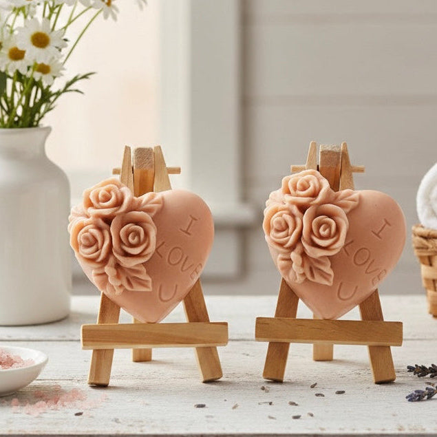Two handmade heart vegan soaps by Soap Simple Creations, embossed with "I Love U" and detailed roses, displayed on wooden easels in a rustic farmhouse decor setting. 