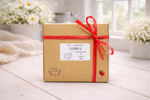 Load image into Gallery viewer, Gift box with red ribbon and 'I Love U' label on a wooden surface with flowers in the background
