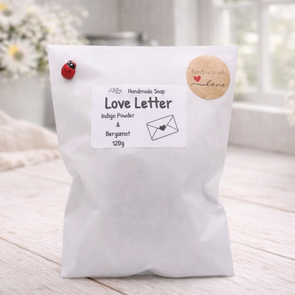 White bag of 'Love Letter' soap with decorative elements on a light wooden surface.
