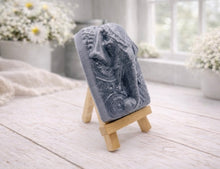 Load image into Gallery viewer, A rectangular handmade vegan soap in a speckled slate-grey finish, featuring a highly detailed relief of an elephant's head adorned with ornate, traditional patterns and a decorative floral background, displayed on a miniature wooden easel.
