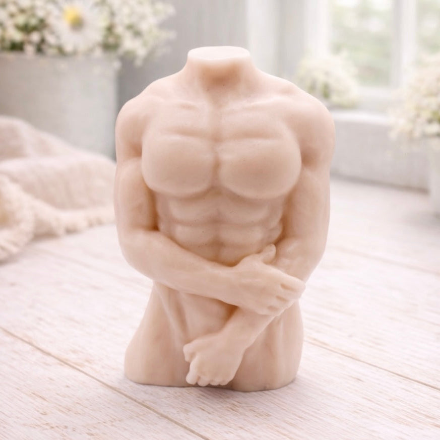 A 3D handmade vegan soap sculpted into a detailed male torso with defined chest and abdominal muscles, finished in a soft tone and displayed in a bright farmhouse setting.