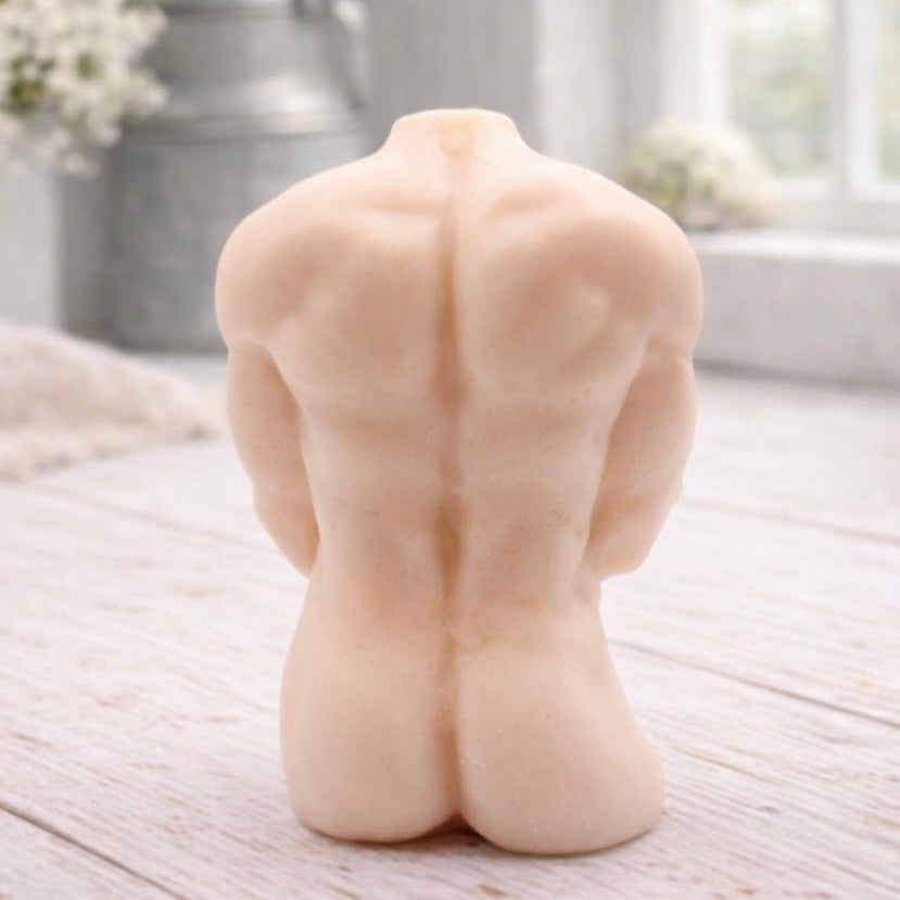 A 3D handmade vegan soap sculpted into a detailed male torso with defined chest and abdominal muscles, finished in a soft tone and displayed in a bright farmhouse setting.