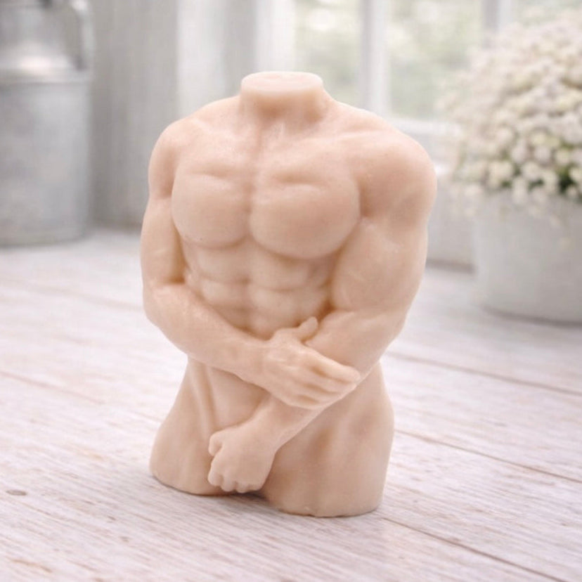 A 3D handmade vegan soap sculpted into a detailed male torso with defined chest and abdominal muscles, finished in a soft tone and displayed in a bright farmhouse setting.