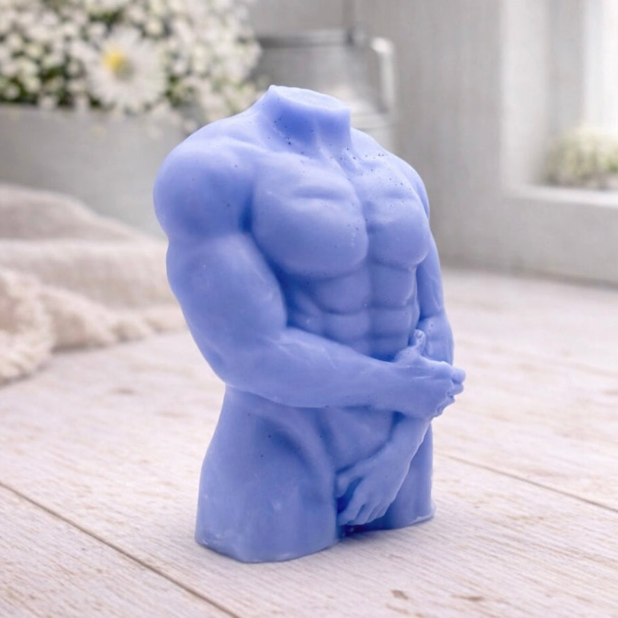 A 3D handmade vegan soap sculpted into a detailed male torso with defined chest and abdominal muscles, finished in a soft tone and displayed in a bright farmhouse setting.