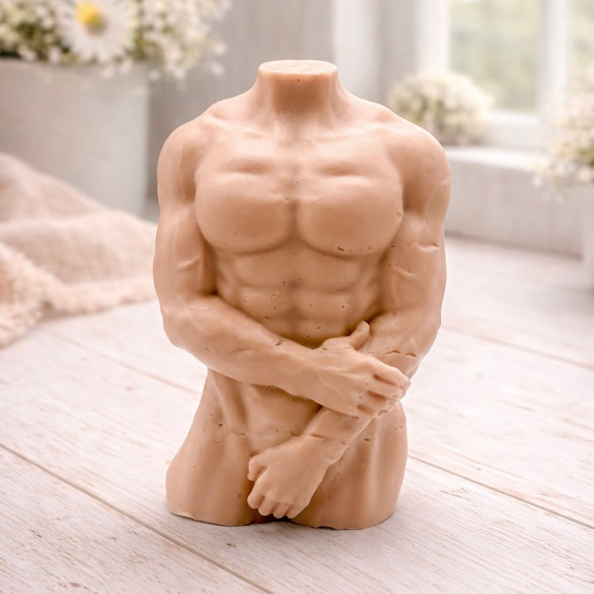 A 3D handmade vegan soap sculpted into a detailed male torso with defined chest and abdominal muscles, finished in a soft tone and displayed in a bright farmhouse setting.