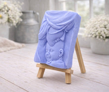Load image into Gallery viewer, A rectangular handmade vegan soap featuring a high-relief carving of a mother tenderly cradling a small baby in her arms, displayed on a miniature wooden easel in a bright farmhouse setting.
