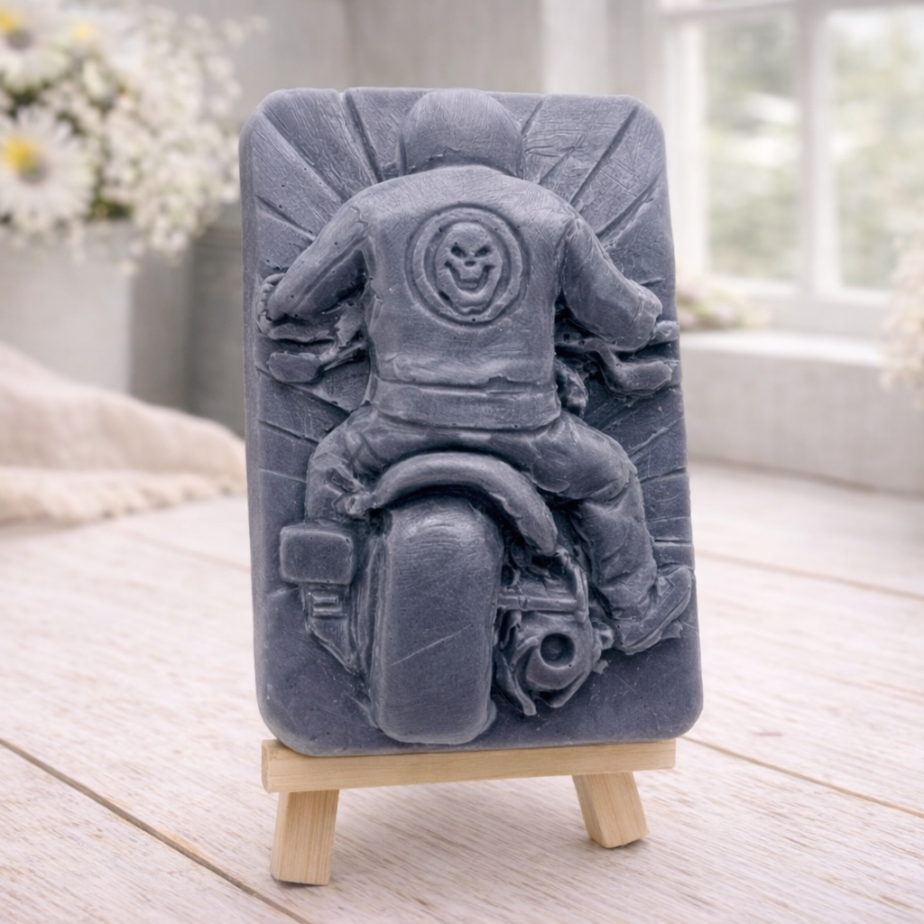 detailed handmade vegan soap gift featuring a motorcycle rider with a skull emblem on their jacket, displayed on a wooden easel against a whimsical farmhouse decor background