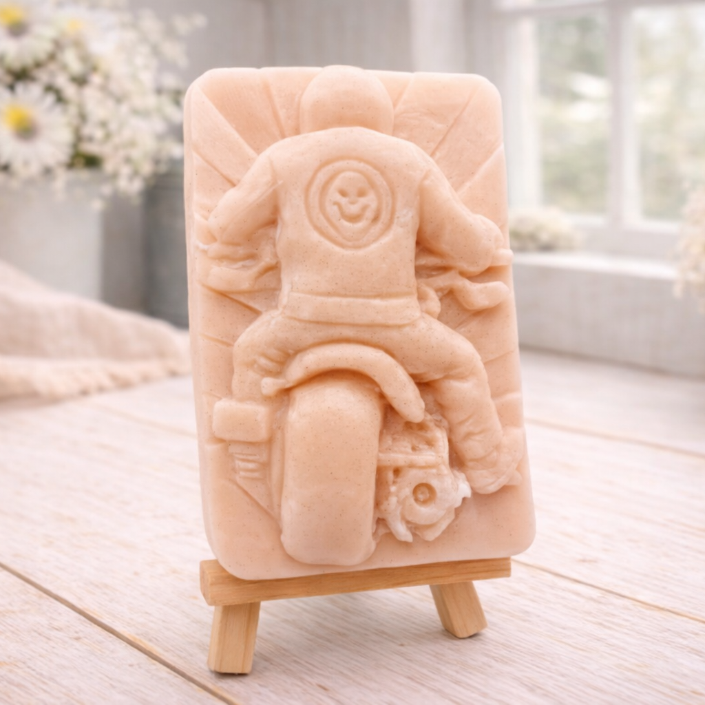 detailed handmade vegan soap gift featuring a motorcycle rider with a skull emblem on their jacket, displayed on a wooden easel against a whimsical farmhouse decor background