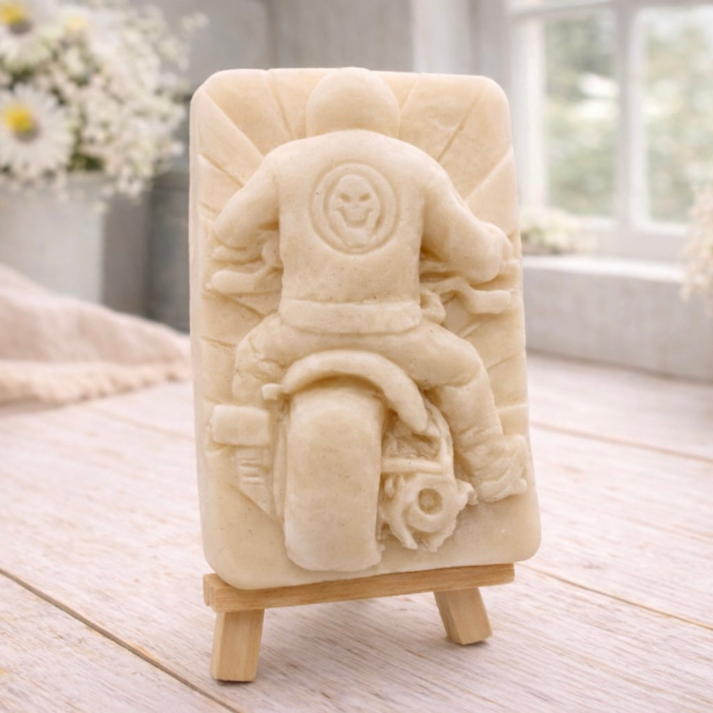 detailed handmade vegan soap gift featuring a motorcycle rider with a skull emblem on their jacket, displayed on a wooden easel against a whimsical farmhouse decor background
