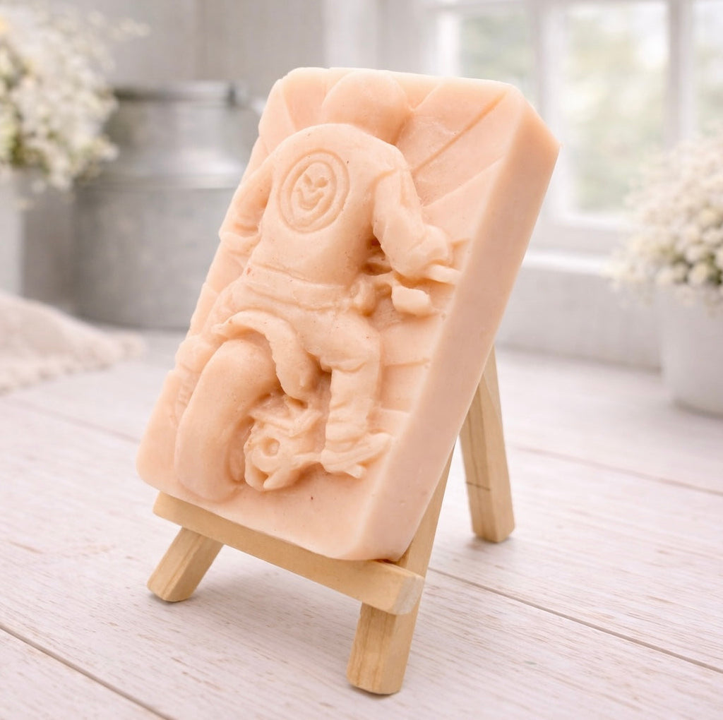 detailed handmade vegan soap gift featuring a motorcycle rider with a skull emblem on their jacket, displayed on a wooden easel against a whimsical farmhouse decor background