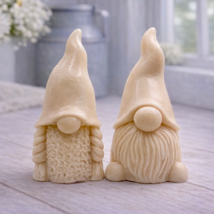 A pair of handmade vegan soaps, featuring a Mr and Mrs Gnome (gonk) set; one with a full textured beard and the other with thick braided plaits, both wearing tall, pointed hats. Gift boxed. 