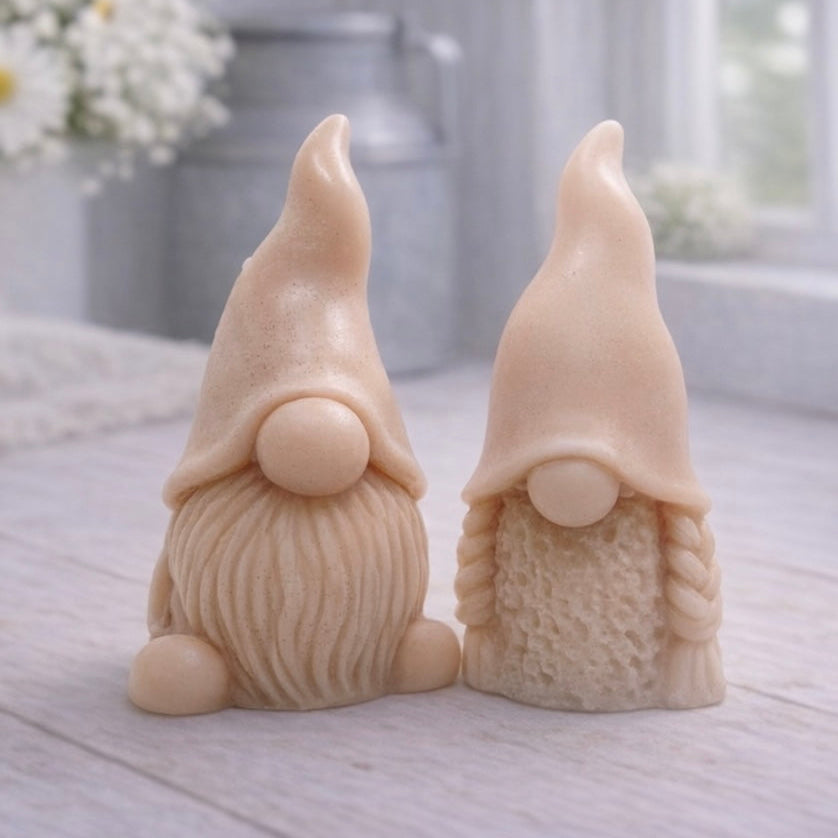 A pair of handmade vegan soaps, featuring a Mr and Mrs Gnome (gonk) set; one with a full textured beard and the other with thick braided plaits, both wearing tall, pointed hats. Gift boxed. 