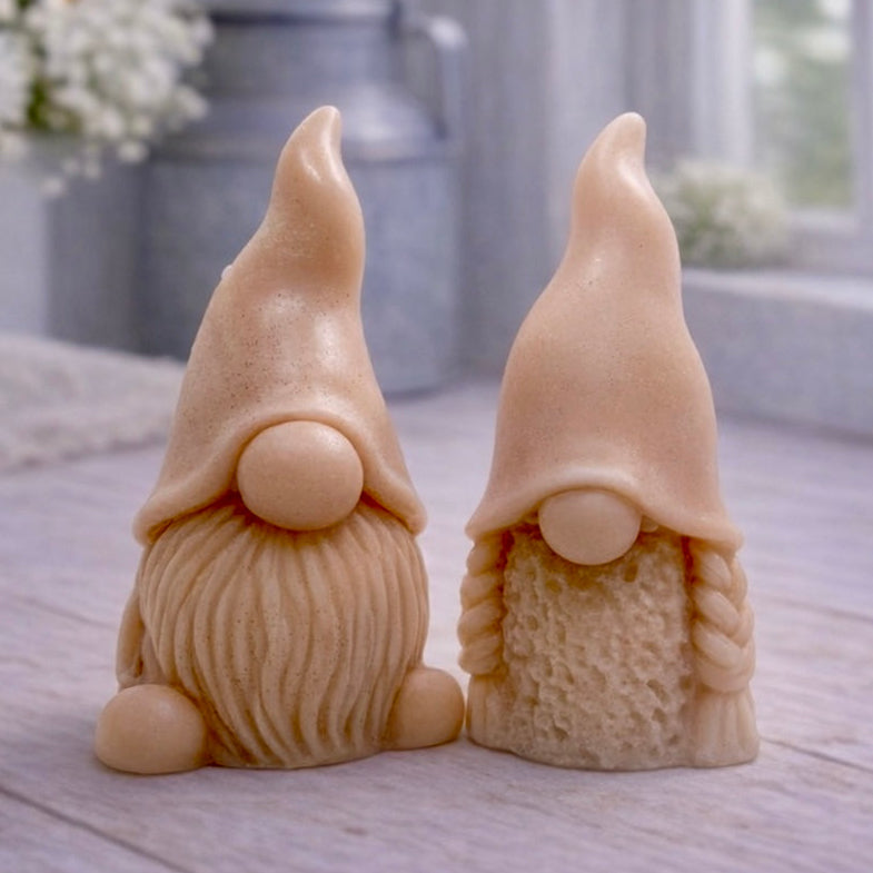 A pair of handmade vegan soaps, featuring a Mr and Mrs Gnome (gonk) set; one with a full textured beard and the other with thick braided plaits, both wearing tall, pointed hats. Gift boxed. 