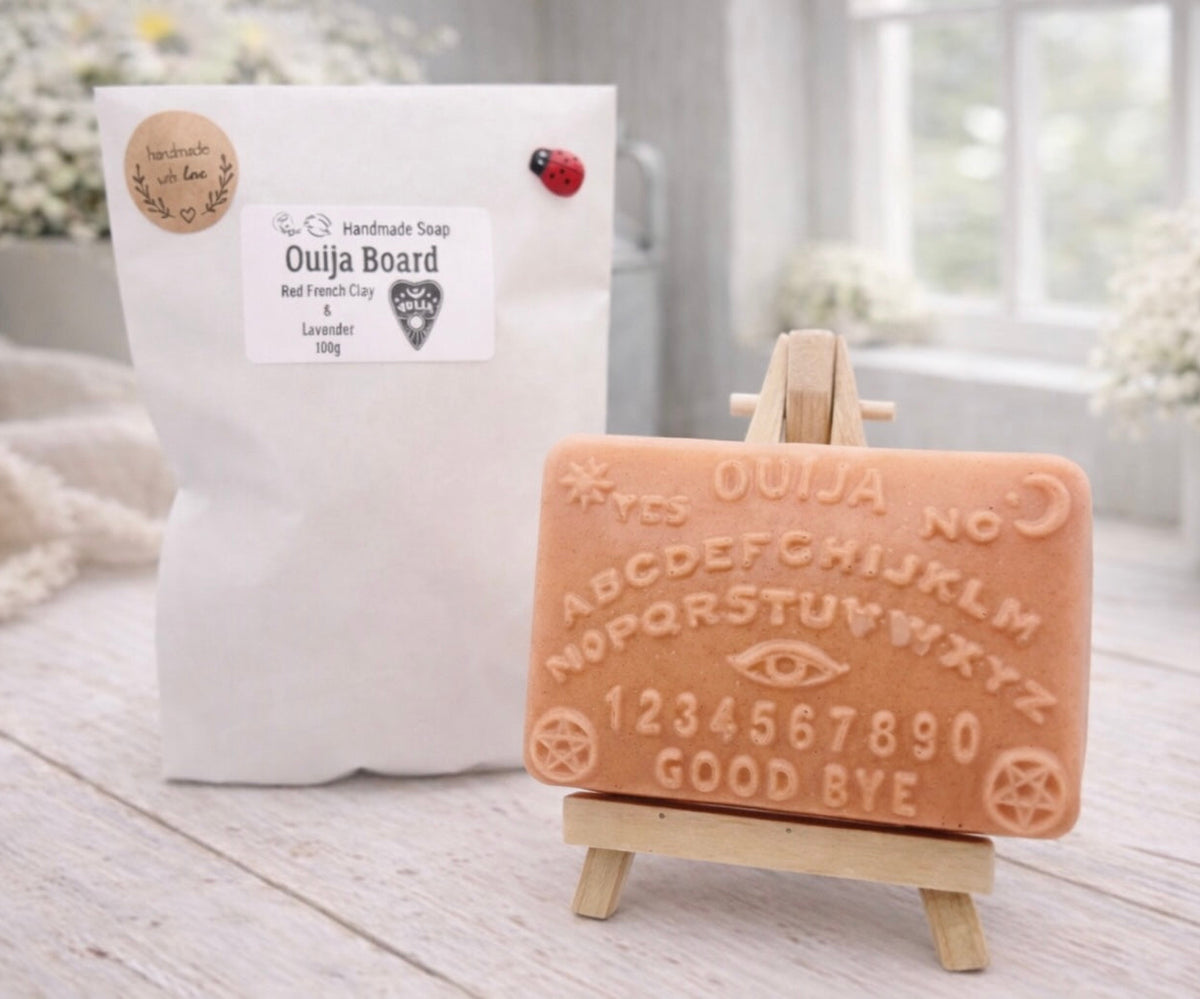 A rectangular handmade vegan soap featuring a highly detailed relief of a classic Ouija spirit board with the alphabet, numbers 0-9, an eye symbol, and the words "Yes," "No," and "Good Bye," displayed on a miniature wooden easel.