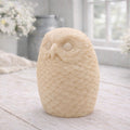 A detailed large handmade vegan soap gift in the shape of an owl with intricate feather textures, displayed on a light wooden table with white flowers in the background.