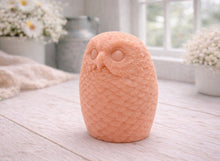 Load image into Gallery viewer, A detailed large handmade vegan soap gift in the shape of an owl with intricate feather textures, displayed on a light wooden table with white flowers in the background.
