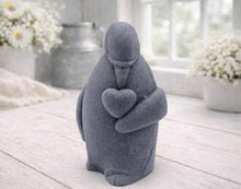Load image into Gallery viewer, A 3D handmade vegan soap sculpted as a standing penguin tenderly cradling a heart against its chest, displayed on a light wooden surface in a bright farmhouse setting.
