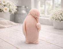 Load image into Gallery viewer, A 3D handmade vegan soap sculpted as a standing penguin tenderly cradling a heart against its chest, displayed on a light wooden surface in a bright farmhouse setting.
