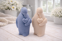 Load image into Gallery viewer, A 3D handmade vegan soap sculpted as a standing penguin tenderly cradling a heart against its chest, displayed on a light wooden surface in a bright farmhouse setting.
