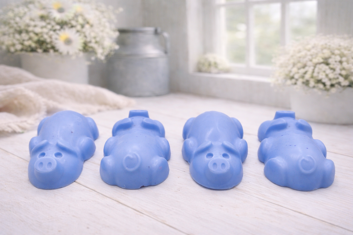 A charming collection of four handmade vegan soaps featuring four piglets, each intricately sculpted with realistic textures and playful expressions, arranged on a light wooden surface.
