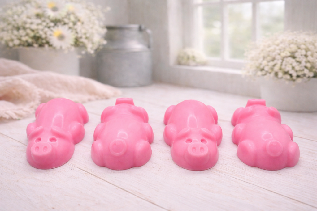 A charming collection of four handmade vegan soaps featuring four piglets, each intricately sculpted with realistic textures and playful expressions, arranged on a light wooden surface.