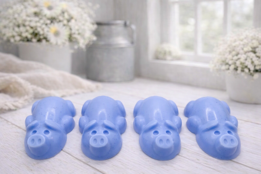 A charming collection of four handmade vegan soaps featuring four piglets, each intricately sculpted with realistic textures and playful expressions, arranged on a light wooden surface.