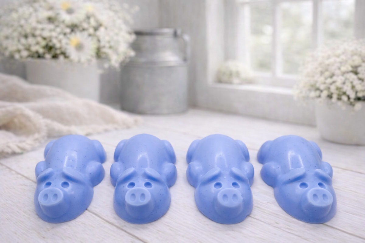 A charming collection of four handmade vegan soaps featuring four piglets, each intricately sculpted with realistic textures and playful expressions, arranged on a light wooden surface.