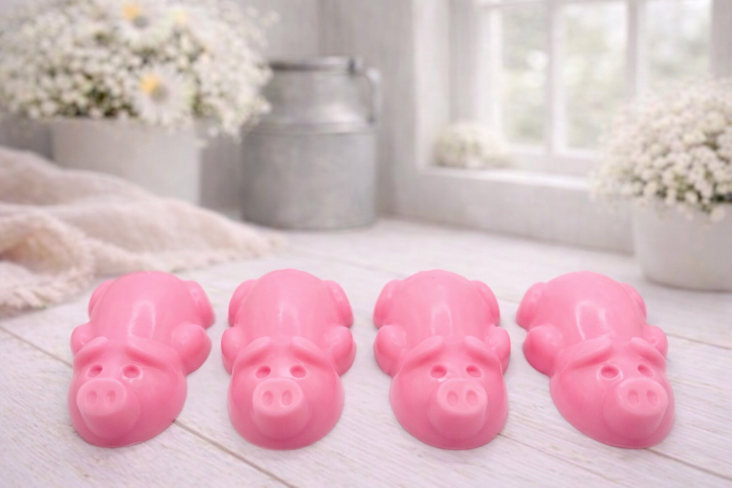 A charming collection of four handmade vegan soaps featuring four piglets, each intricately sculpted with realistic textures and playful expressions, arranged on a light wooden surface.