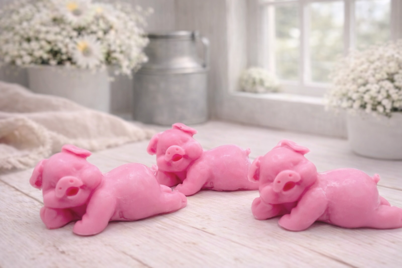 Three cute laughing pig-shaped vegan soap gift set on a wooden surface with flowers in the background