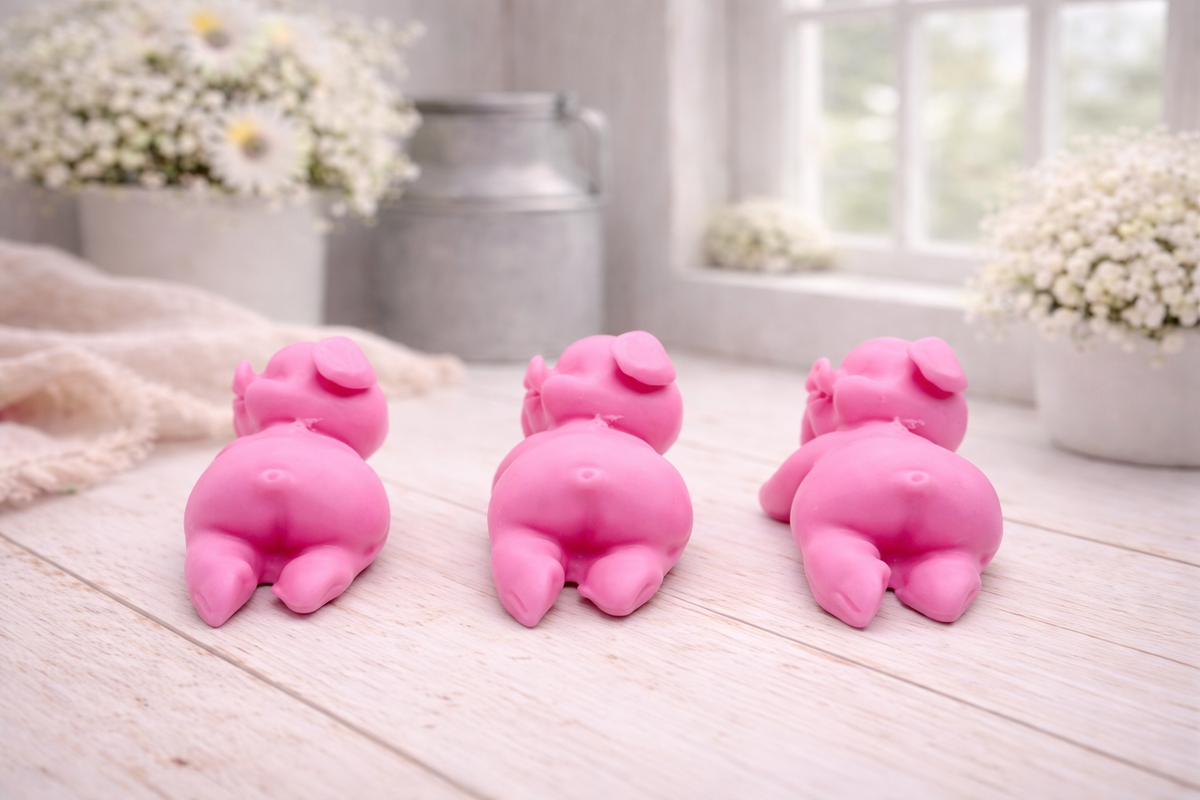 Three cute laughing pig-shaped vegan soap gift set on a wooden surface with flowers in the background