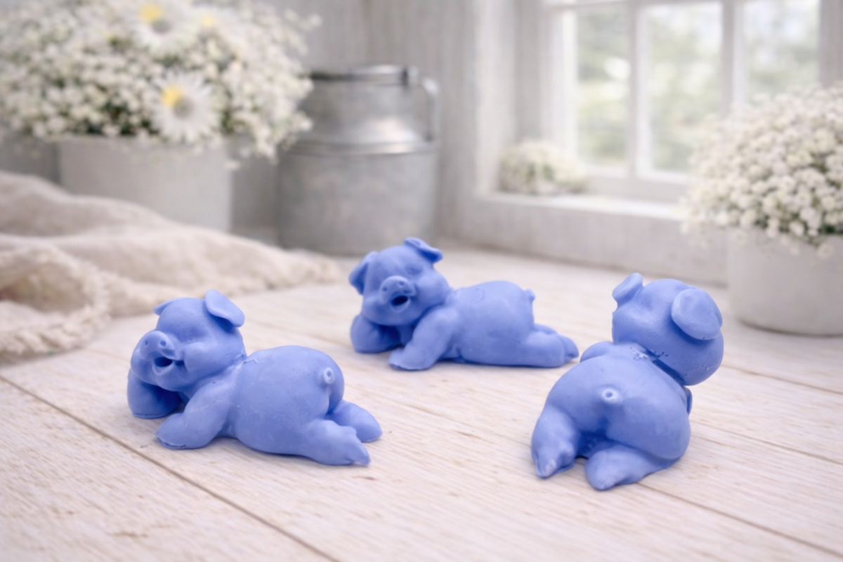 Three cute laughing pig-shaped vegan soap gift set on a wooden surface with flowers in the background