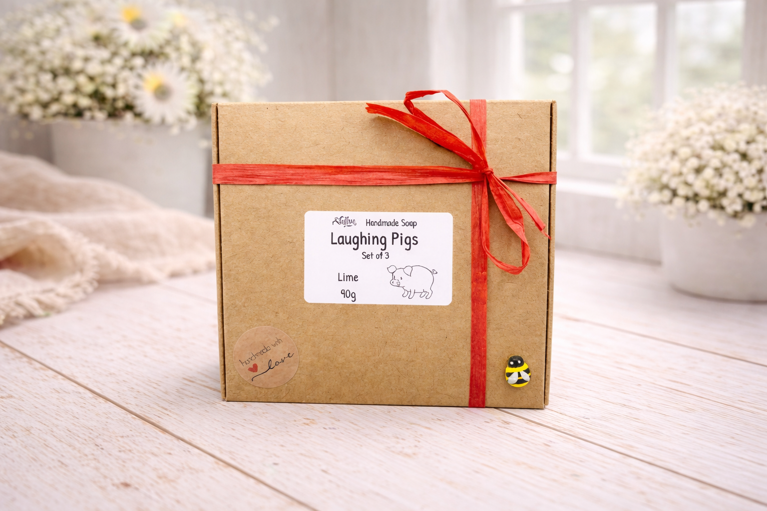 Kraft paper gift box with red ribbon and 'Laughing Pigs' label on a wooden surface.